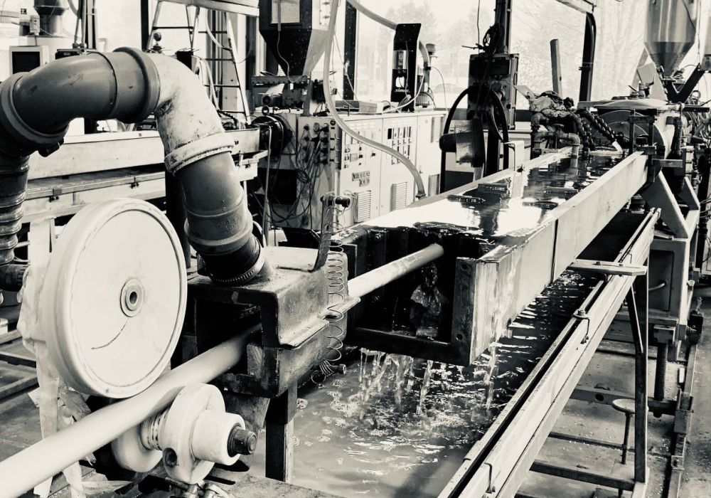 Lohnfertigung - Extrusion - die gesamte Extrusionsanlage ist zu sehen, Kunststoff wird im Extruderer erhitzt und über eine Förderschnecke weiterbefördert und in Form gebracht, anschließend im Wasserbad abgekühlt