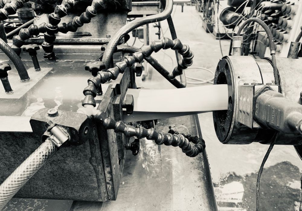 Herstellung von Kunststoffprofilen durch Extrusion. Auf dem Bild sieht man wie Kunststoff durch den Extrudierer hindurch in das Abkühlbecken gelangt.